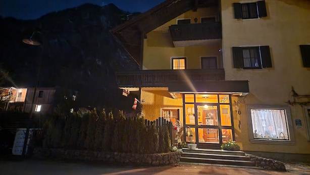 A two-story building with a balcony, a stone wall, and a mountain in the background. - Rosy's House Pension Privatzimmer (Bad Goisern)