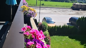 A balcony with flower boxes and a view of a road with cars and houses in the background. - Rosy's House Pension Privatzimmer (Bad Goisern)