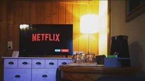 A room with a television displaying the Netflix logo, a wooden cabinet, a lamp, and a coffee maker. - Rosy's House Pension Privatzimmer (Bad Goisern)