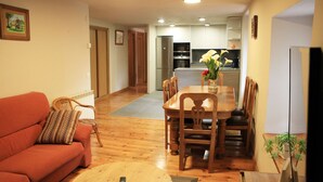 Una sala de estar con un sofá, una mesa de centro y una mesa de comedor con sillas. Se ve una cocina al fondo.
