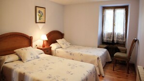Un dormitorio con dos camas individuales, una mesita de noche con lámpara, una silla y una ventana con cortinas de encaje.