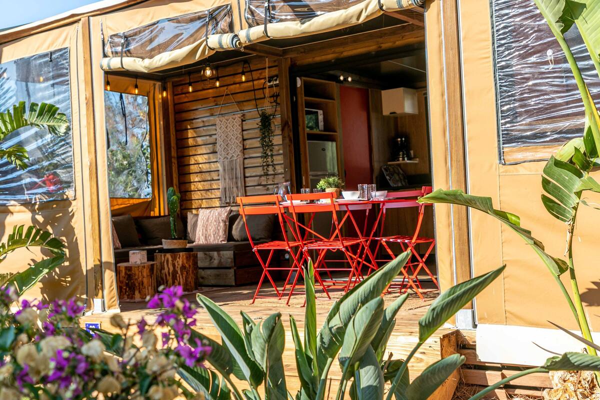 Een knus buitenverblijf met een houten tafel en rode stoelen, omgeven door potplanten en een houten terras.