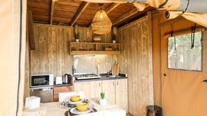 A compact kitchen with wooden walls, a dining table with yellow bowls, a microwave, a stove, and a hanging light fixture. - Camping Site de Gorge Vent (Fréjus)