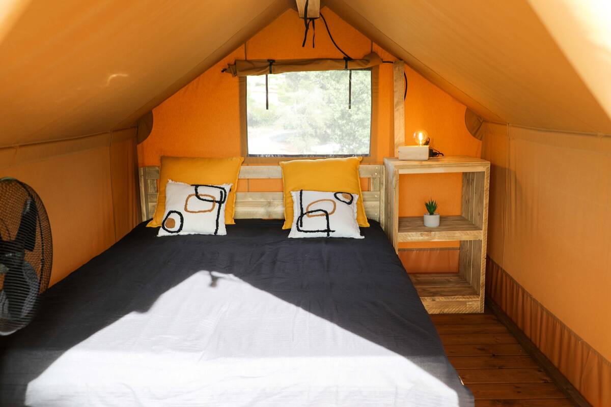 Een gezellig slaapkamer op zolder met een bed, kussens, een klein tafeltje en een ventilator.