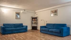 Une pièce avec deux canapés bleus, une bibliothèque et un tableau accroché au mur.