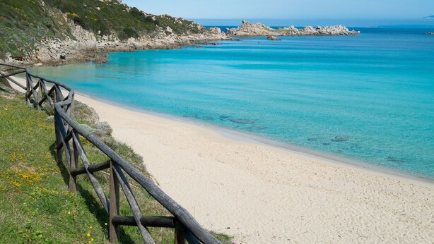 Une plage à l’eau turquoise et limpide, un rivage sablonneux et, au loin, des formations rocheuses.