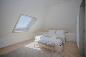 A bedroom with a skylight, a bed, a bedside table, and a bench.