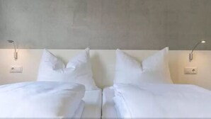 A hotel room with a large bed, two bedside tables, and a plain wall. - a2 Hotels Wernau (Wernau)