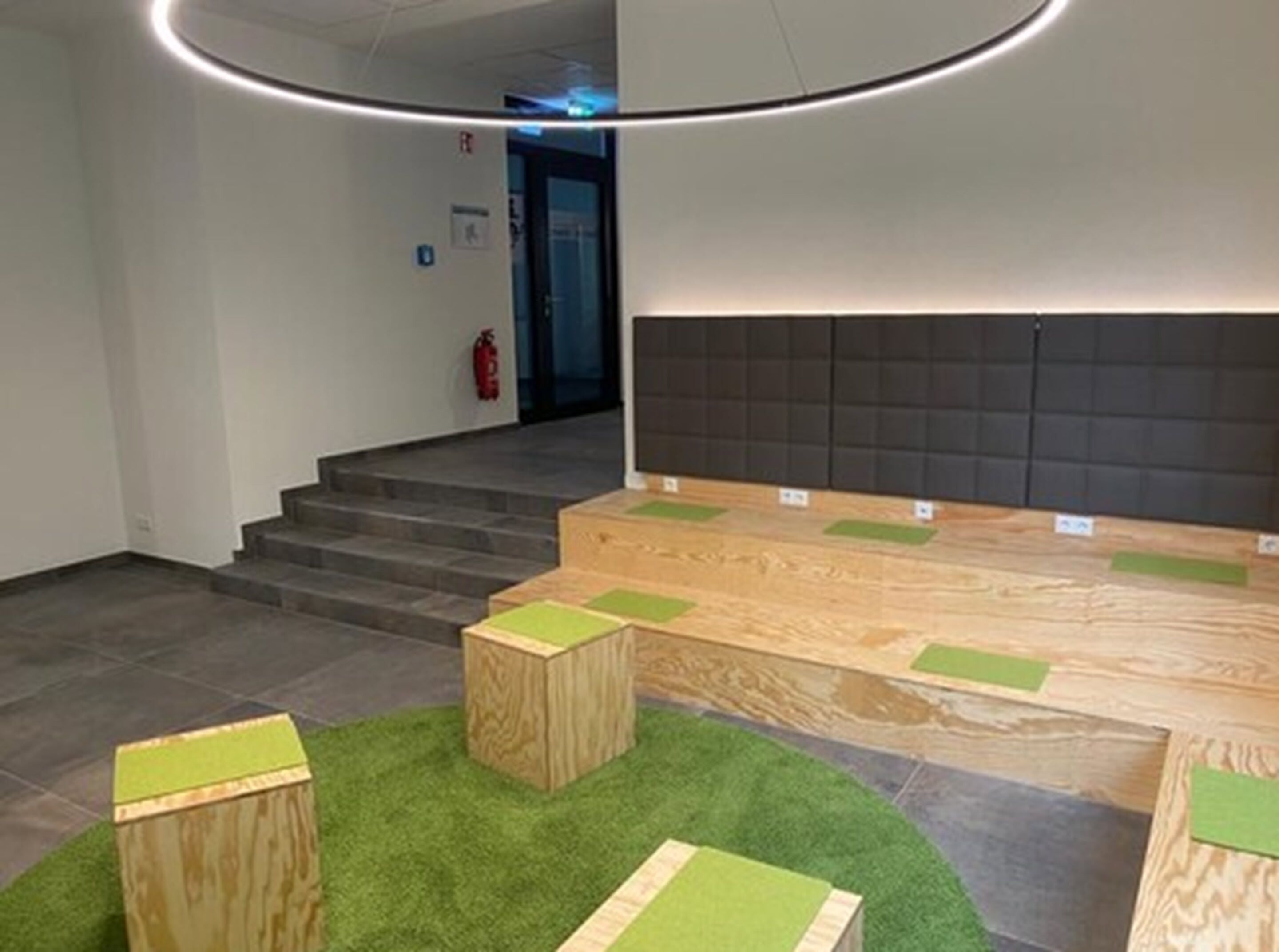 Un interior moderno con una recepción, una escalera y un área de descanso con cojines verdes.