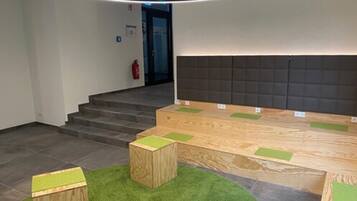 Un interior moderno con una recepción, una escalera y un área de descanso con cojines verdes.