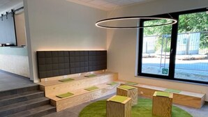 A modern waiting area with a grey padded bench, a green carpet, and a large window with a view of the outside. - a2 Hotels Wernau (Wernau)