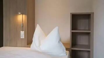 A hotel room with a bed, a wall-mounted light, and a wooden shelf unit.