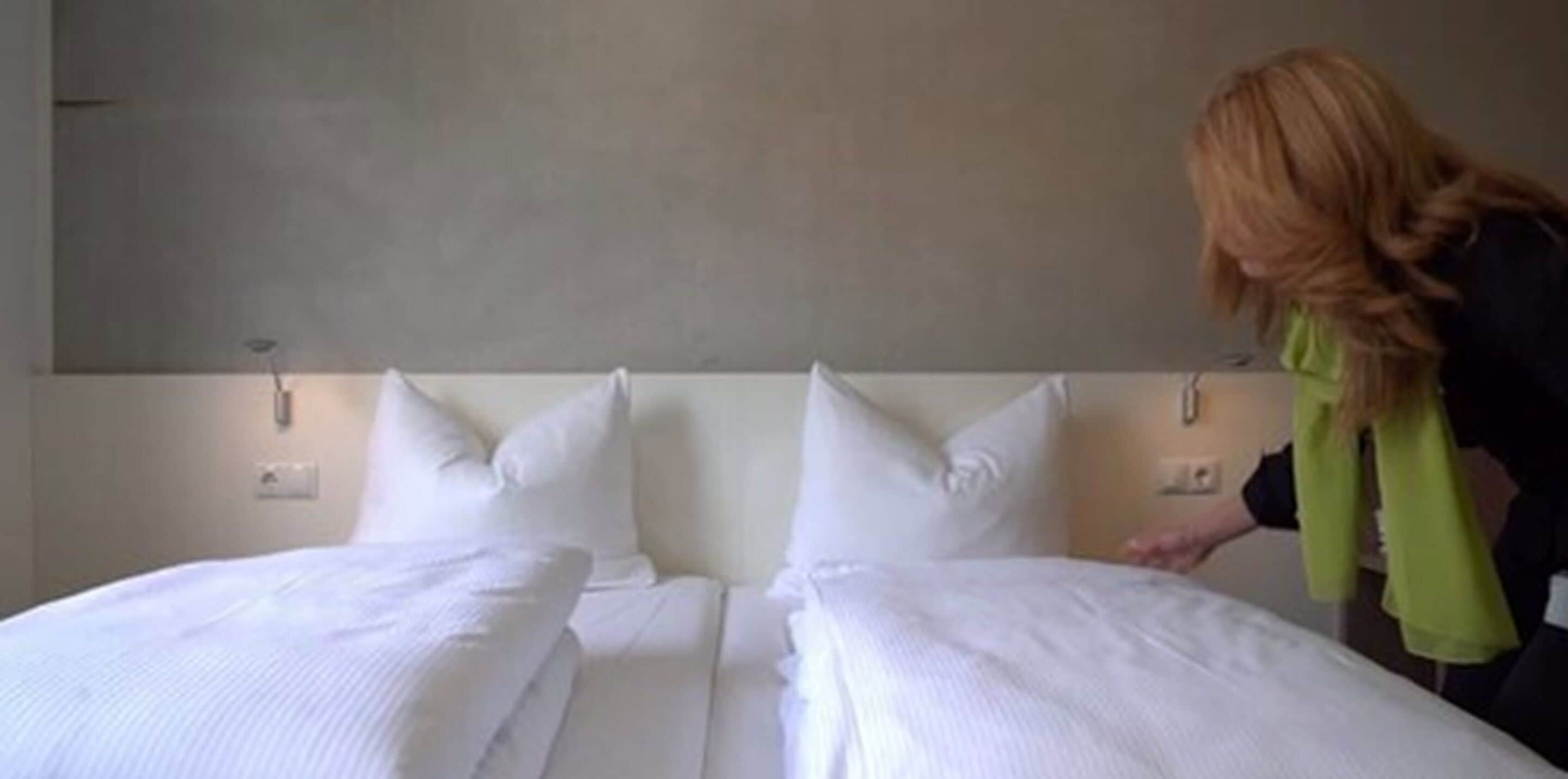 Habitación de hotel con dos camas, cada una con ropa de cama y almohadas blancas, y cabeceros de color neutro.