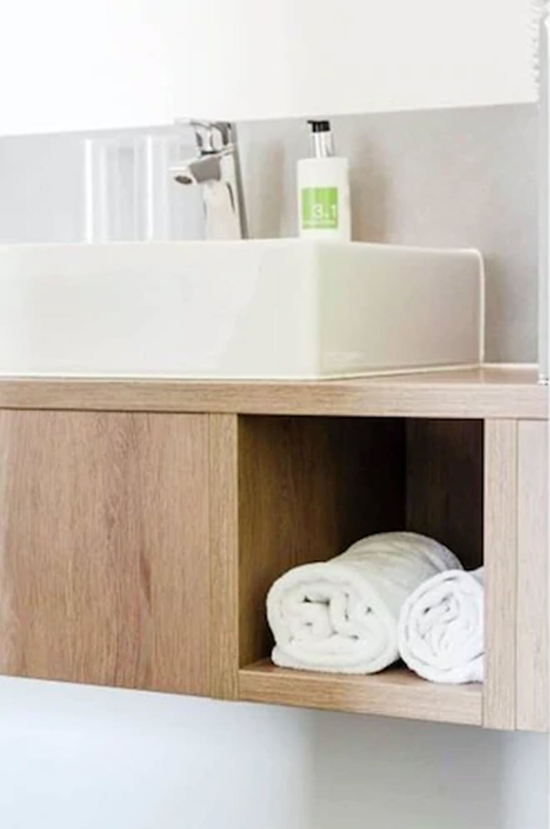 Un bagno con un lavandino bianco, uno scaffale in legno e una bottiglia di sapone per le mani.