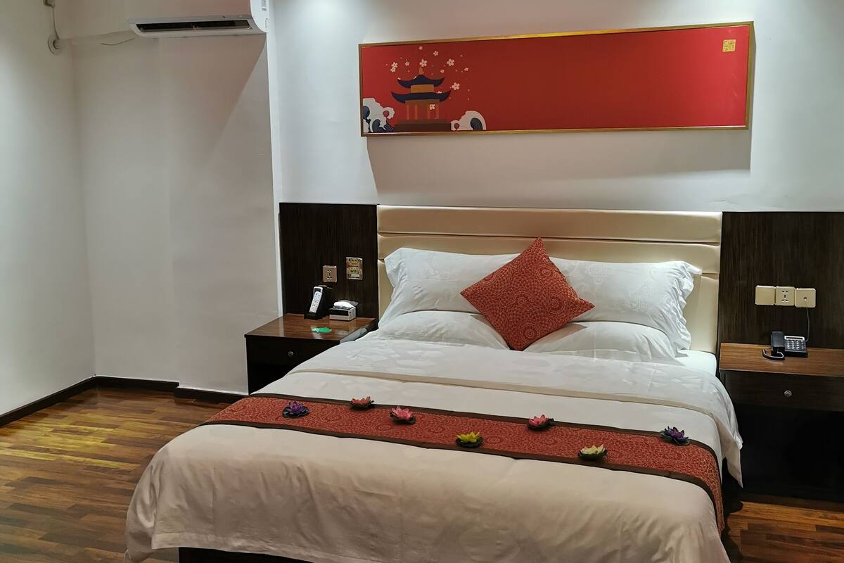Una habitación de hotel con una cama grande, un candelabro, una obra de arte roja en la pared y suelo de madera.