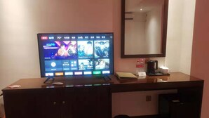 Une chambre d’hôtel équipée d’une télévision diffusant un programme, d’une machine à café, d’une poubelle et d’un miroir mural.
