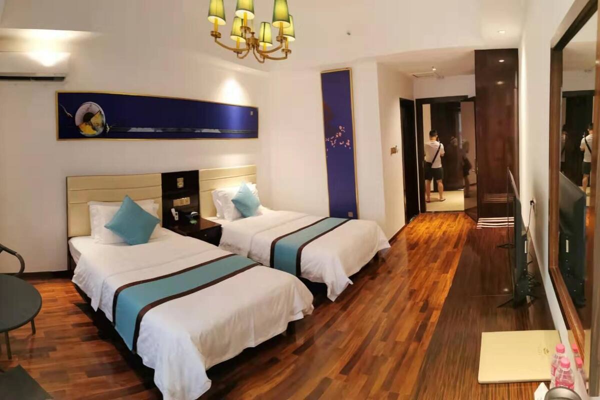 Habitación de hotel con dos camas, un escritorio, una silla, una araña y un espejo grande.
