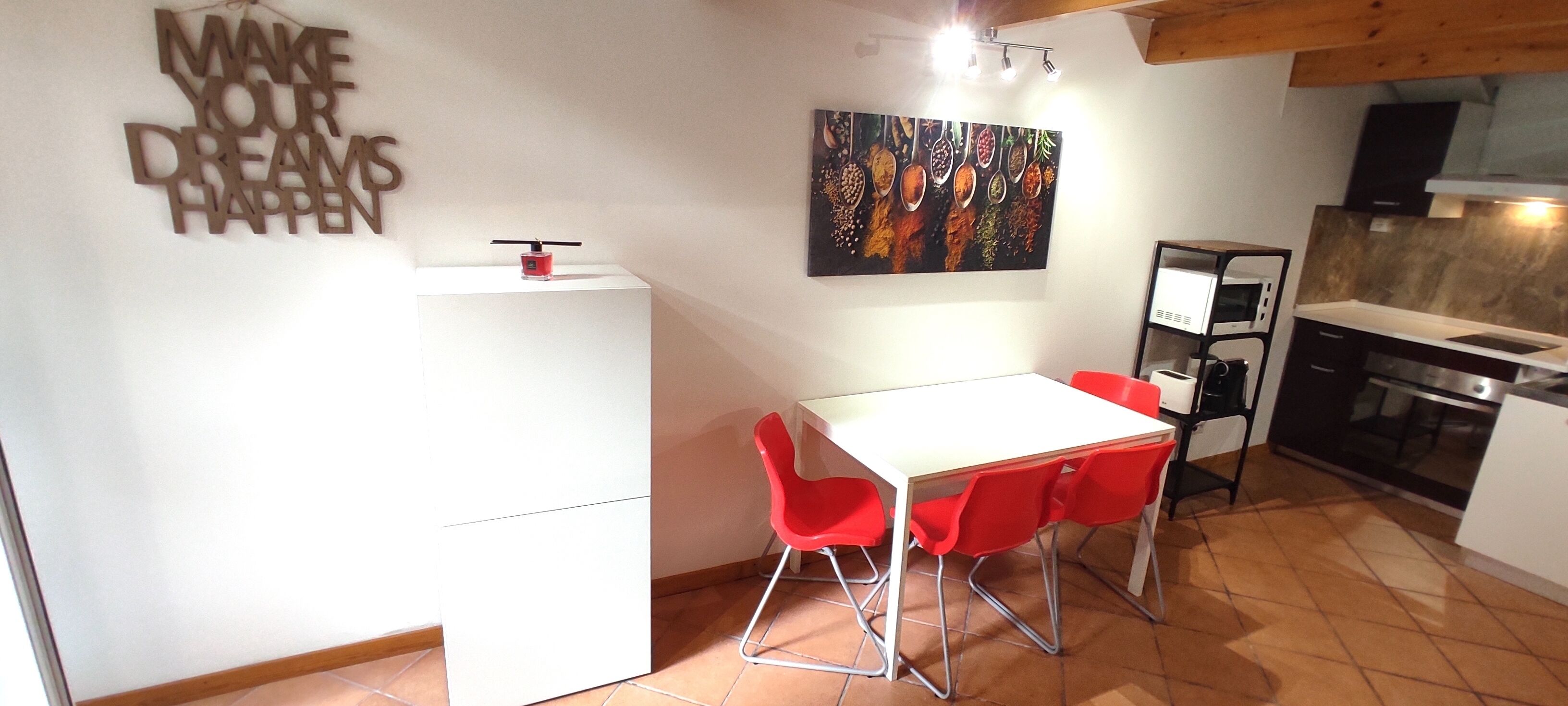 A compact kitchen with a white refrigerator, a dining table with red chairs, and a microwave.