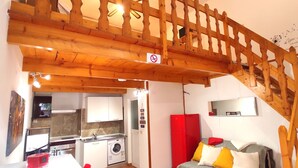 Ein kompakter Wohnraum mit einer Küche, einer Waschmaschine, einem roten Kühlschrank und einer Treppe mit Holzwand.