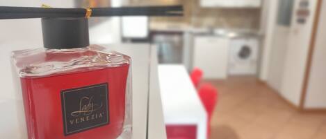 A bottle of Lady Venezia perfume with a black cap and a gold label, placed on a white surface in a modern kitchen with white cabinets and a wooden floor.