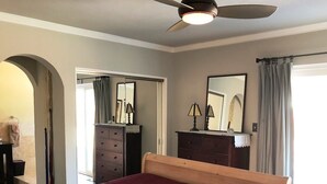 Een slaapkamer met een groot bed, een dressoir, een spiegel en een plafondventilator.