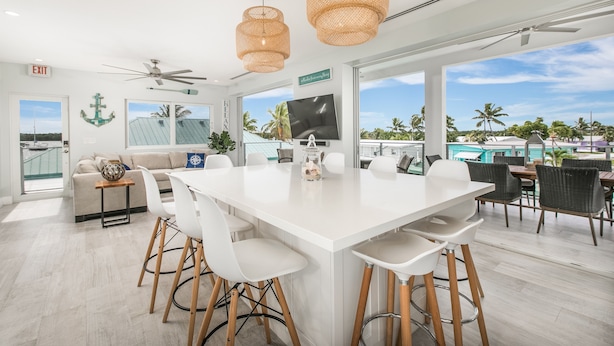 Una cocina moderna con una isla grande, sillas blancas y un ventilador de techo.