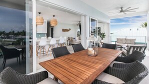 Un comedor amplio con una mesa de madera y sillas de mimbre, ventanas grandes y un ventilador de techo.