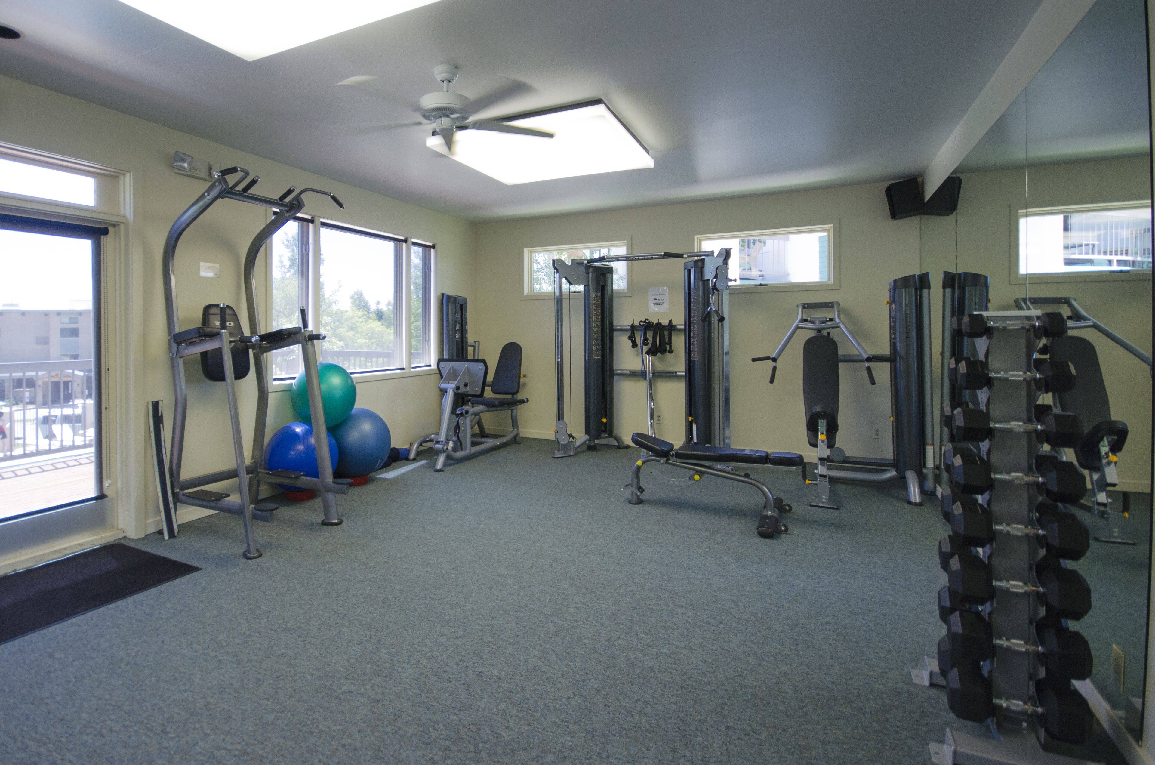 A gym with exercise equipment, a ceiling fan, and large windows.
