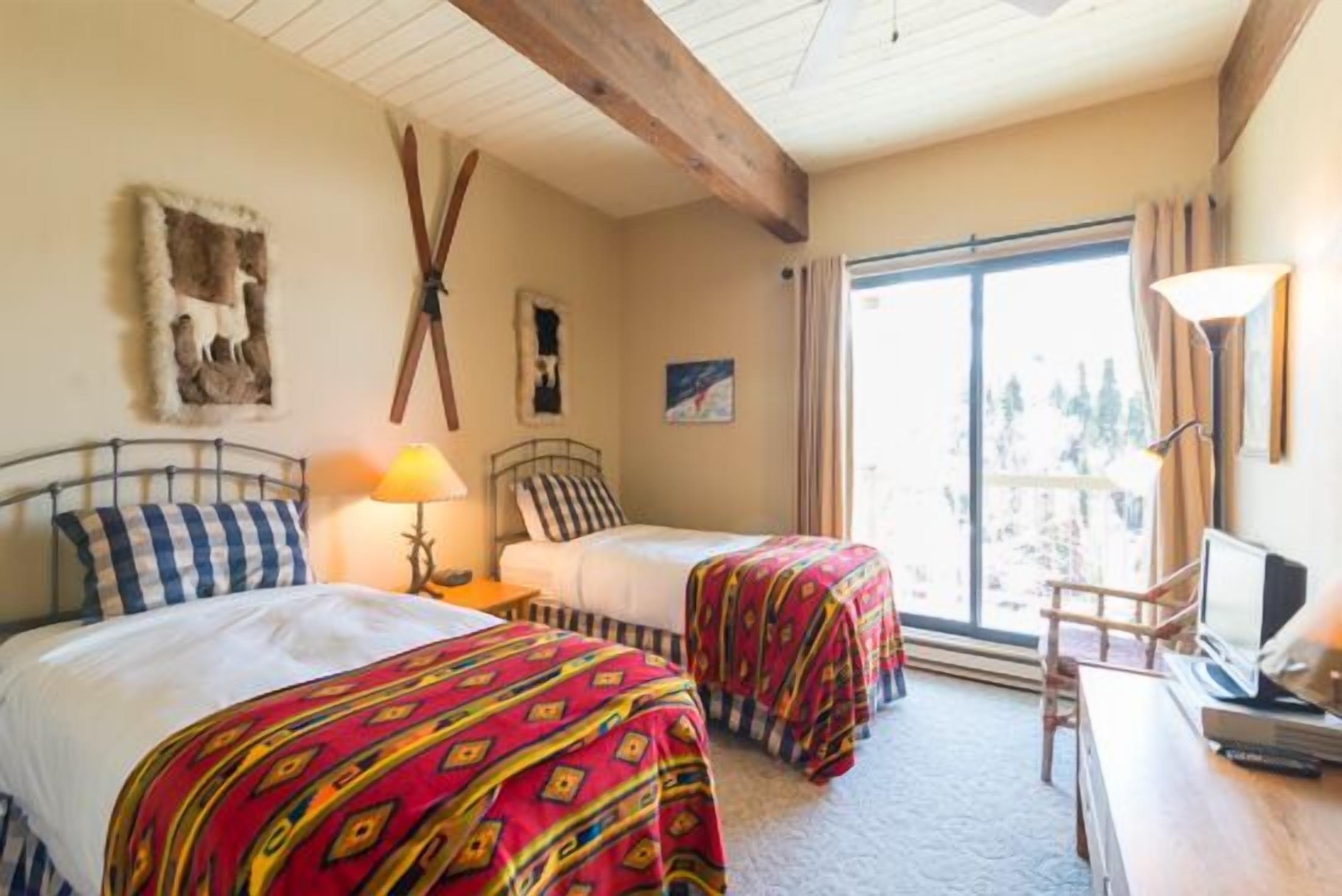 A room with two beds, a desk, and a large window.