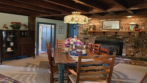 Une salle à manger avec une table en bois, des chaises, un lustre, une cheminée et un mur en briques.