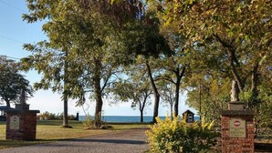 Un chemin pavé mène à un bâtiment dont l’entrée est en briques, entouré d’arbres et offrant une vue sur la mer.