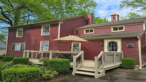 Une maison à deux étages, avec une façade rouge, un porche à l’avant surmonté d’un parasol beige et un petit escalier menant à l’entrée.