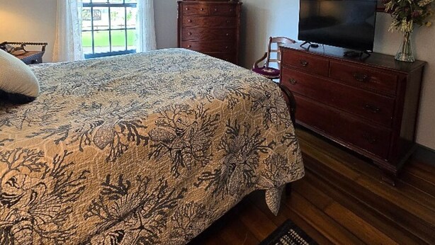 Un dormitorio con cama, cómoda, televisor y ventilador de techo.