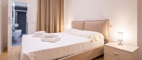 A neatly arranged hotel room with a bed, bedside table, and a view of the bathroom.