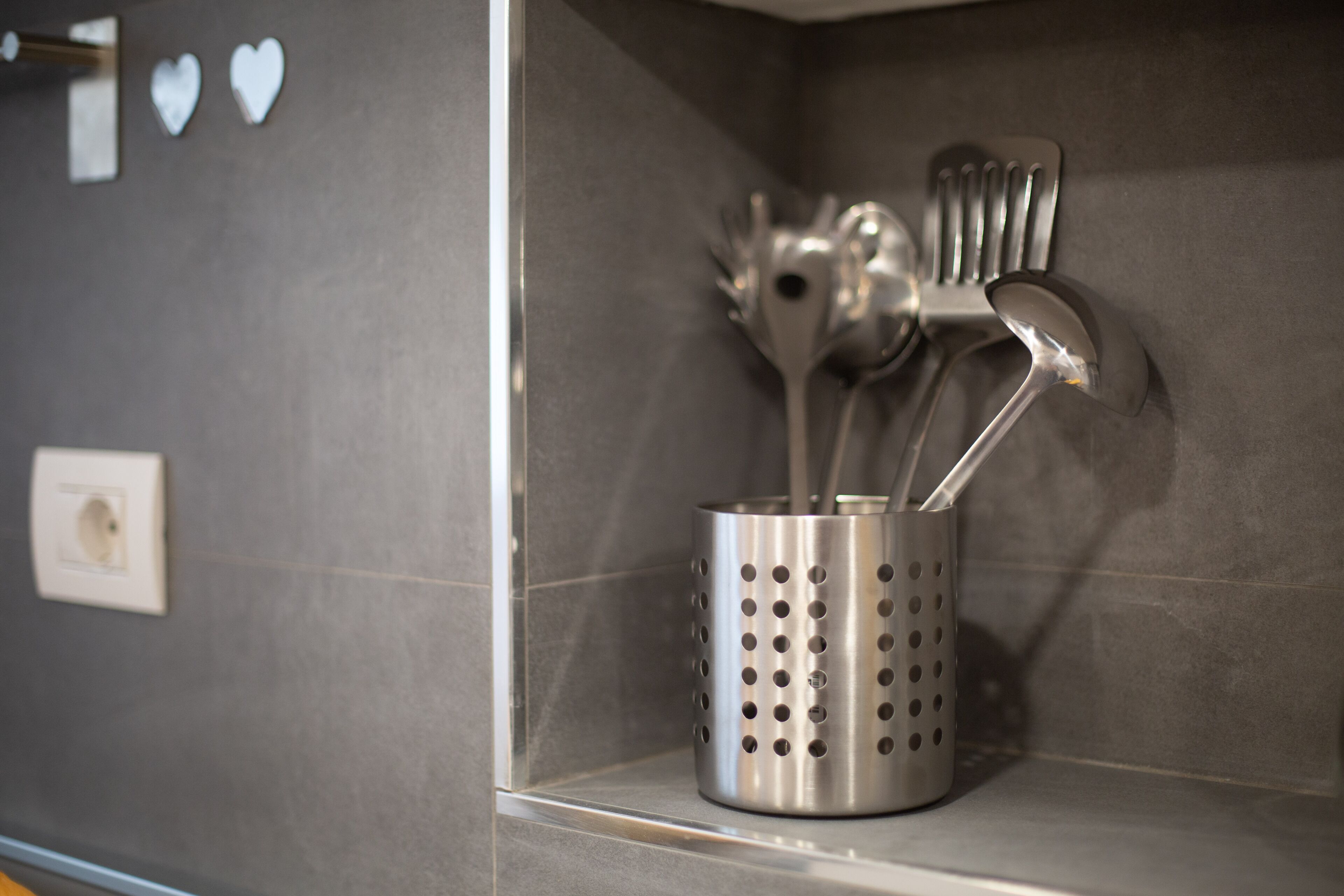 Een metalen bestekhouder met lepels en een spatel op een betegelde muur.