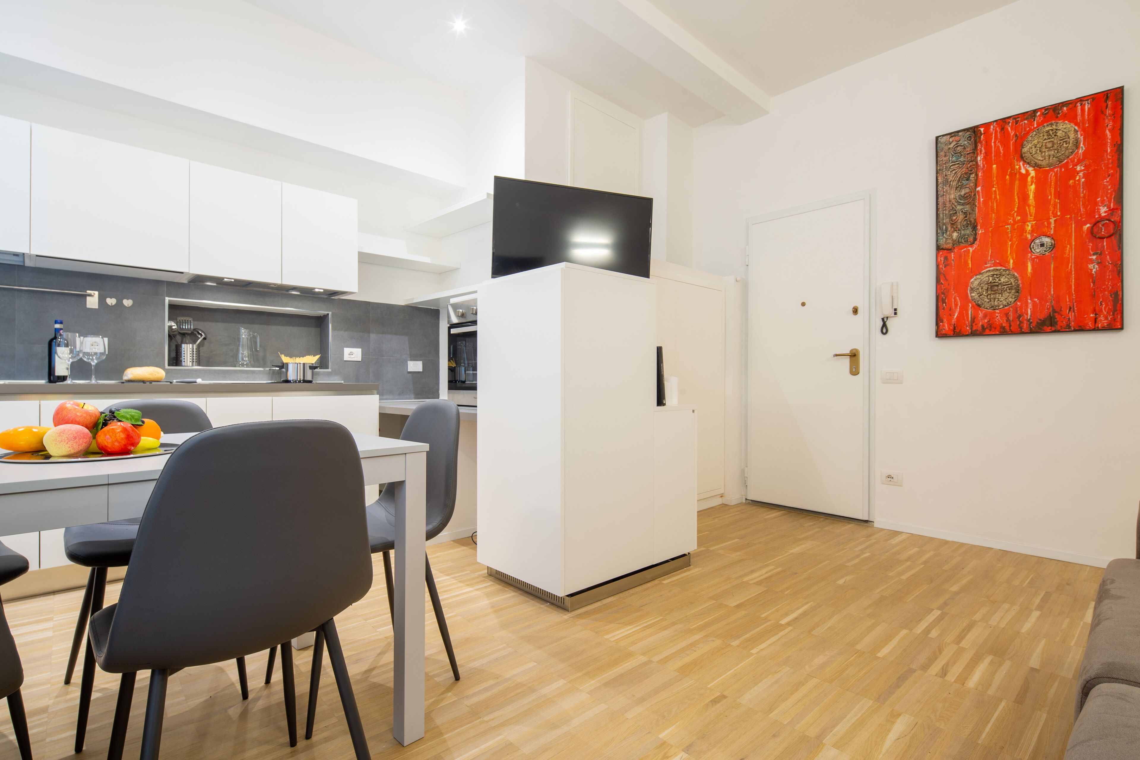 Une cuisine moderne avec des meubles blancs, un coin repas avec une table et des chaises, et un salon avec un canapé.