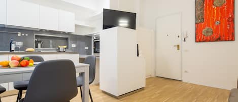 Una cocina moderna con armarios blancos, un comedor con mesa y sillas, y una sala de estar con sofá.
