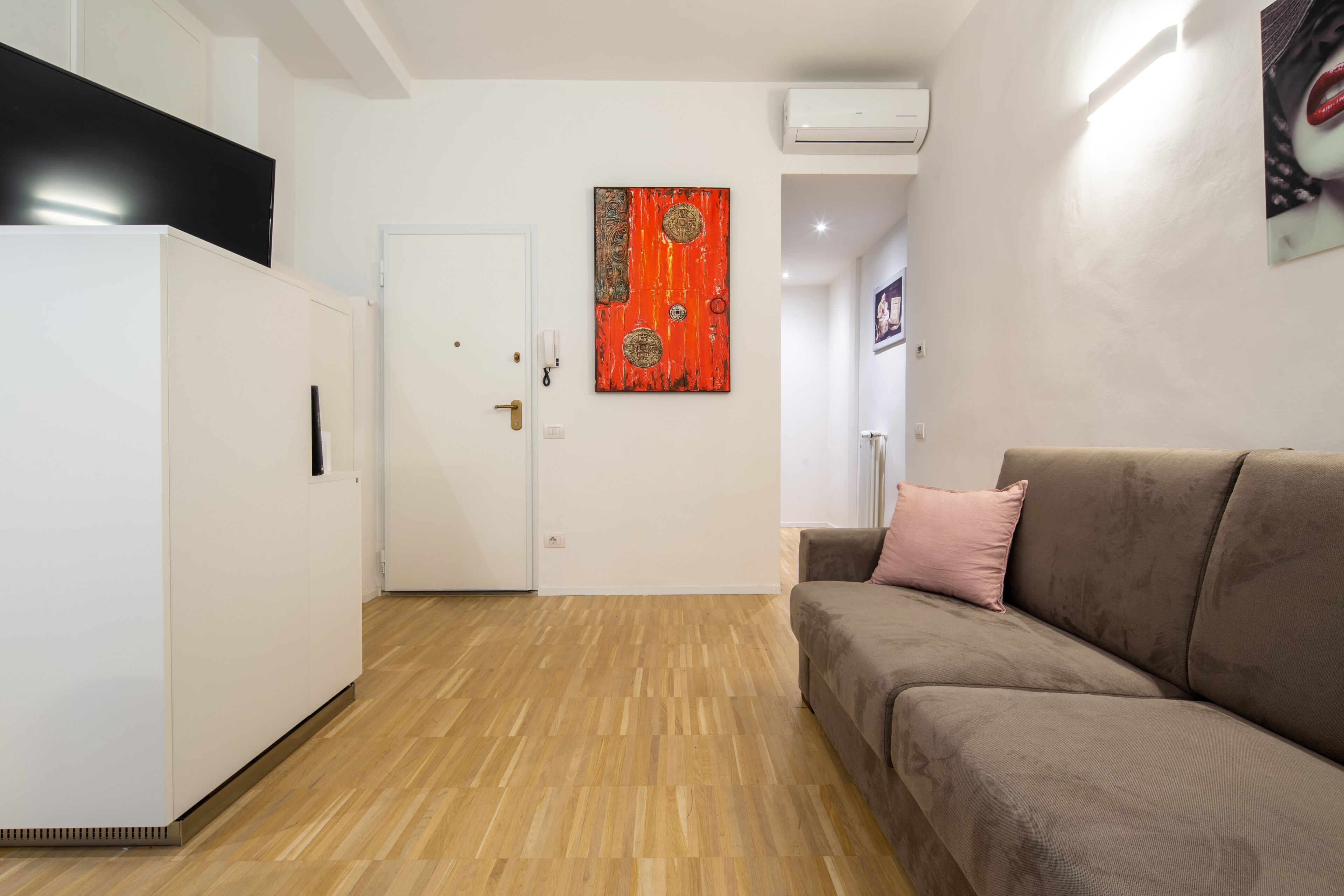A modern living room with a brown sofa, a white door, and a red artwork on the wall.