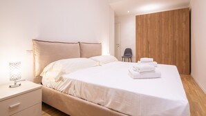 Ein modernes Schlafzimmer mit einem großen Bett, einem Nachttisch, einem Sessel und einem Holzschrank.
