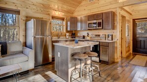 A wooden cabin interior with a kitchen, a sofa, and a bar area. - Cozy Rose` cabin for up to 6 guests - Hocking Hills - Hot Tub-Fire Pit-Wifi (Logan)