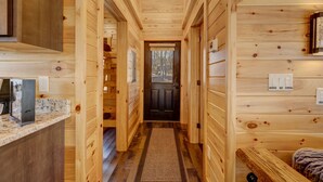 A wooden interior with a hallway leading to a door, a kitchen area with granite countertops, and a bed with a headboard. - Cozy Rose` cabin for up to 6 guests - Hocking Hills - Hot Tub-Fire Pit-Wifi (Logan)