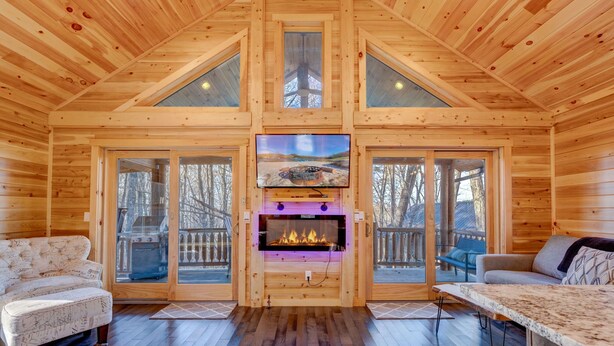 A cozy cabin interior with a fireplace, wooden walls, and a television mounted above it. - Cozy Rose` cabin for up to 6 guests - Hocking Hills - Hot Tub-Fire Pit-Wifi (Logan)
