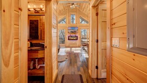 A wooden interior hallway with a fireplace, a ceiling fan, and a TV screen. - Cozy Rose` cabin for up to 6 guests - Hocking Hills - Hot Tub-Fire Pit-Wifi (Logan)