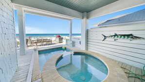 A pool area with a hot tub, outdoor seating, and a view of the ocean.
