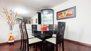 A dining area with a glass table, four chairs, a vase with flowers, and a framed abstract painting on the wall. - Suite Miraflores. A. (Urb Cercado de Miraflores)