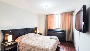 A hotel room with a large bed, a flat-screen TV mounted on the wall, and a window with curtains. - Suite Miraflores. A. (Urb Cercado de Miraflores)