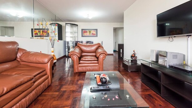 A living room with a leather sofa, a glass coffee table, and a flat-screen TV. - Suite Miraflores. A. (Urb Cercado de Miraflores)