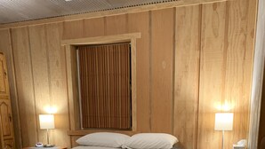 A room with a large bed, two bedside tables with lamps, a wooden headboard, and a window with curtains.