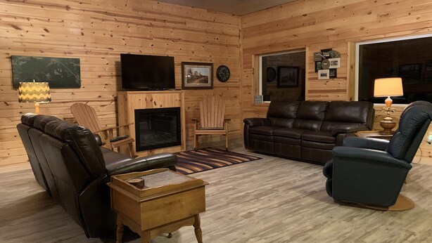 A cozy log cabin interior with a fireplace, leather furniture, and a television.