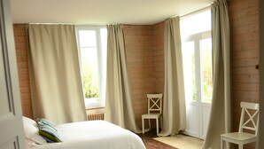 A bedroom with two beds, wooden flooring, a window with curtains, and a chair. - Large bright house in the shape of a boat (Port-en-Bessin-Huppain)